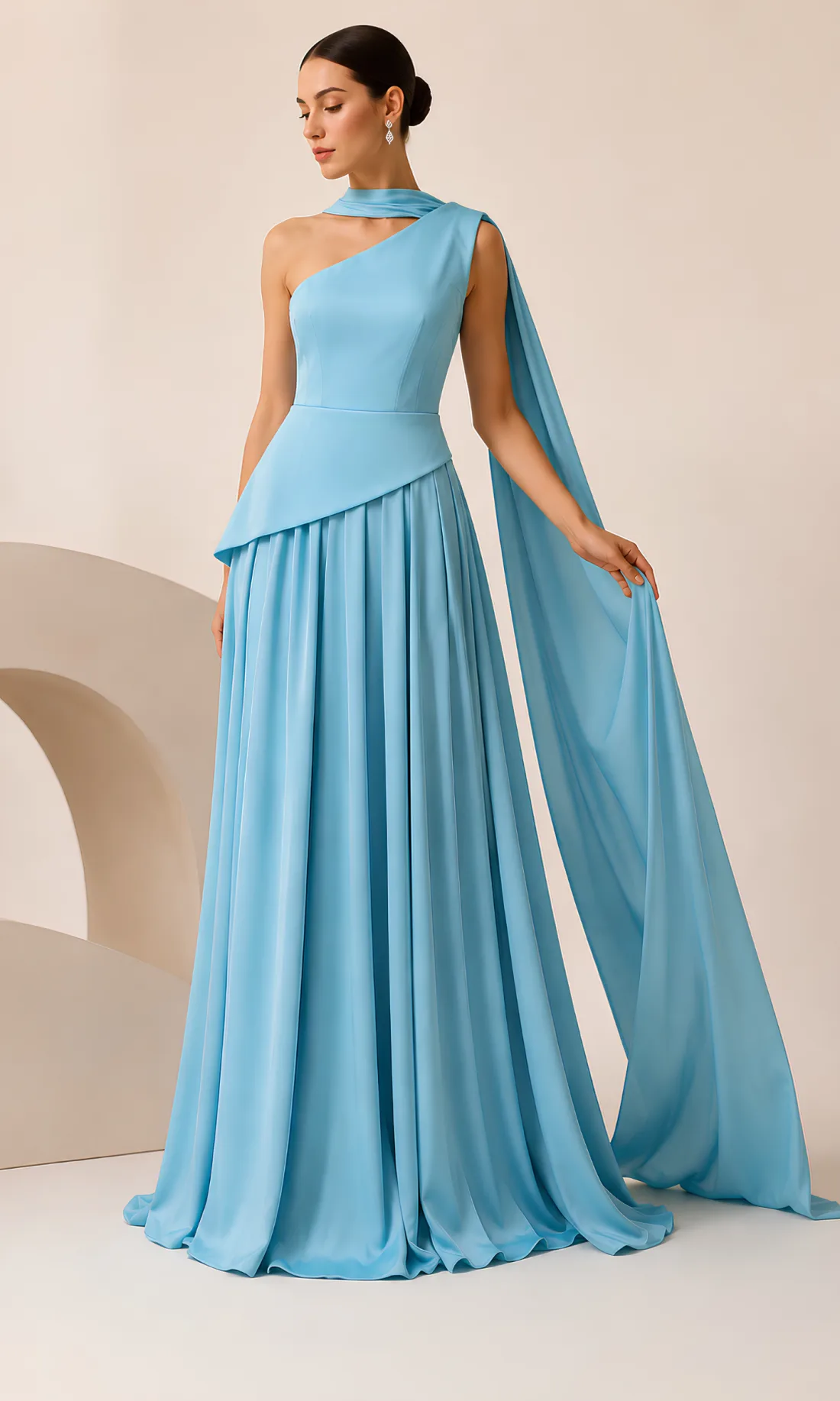 A model wearing the Joie Couture sky blue one-shoulder gown with a long draped cape sleeve, photographed against a pale studio ground